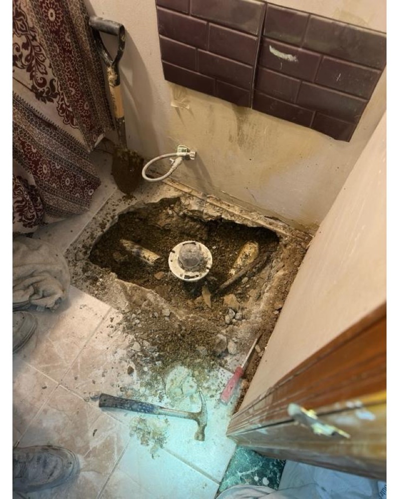 Bathroom floor opened up around a failed closet flange, dirt and tools in the hole